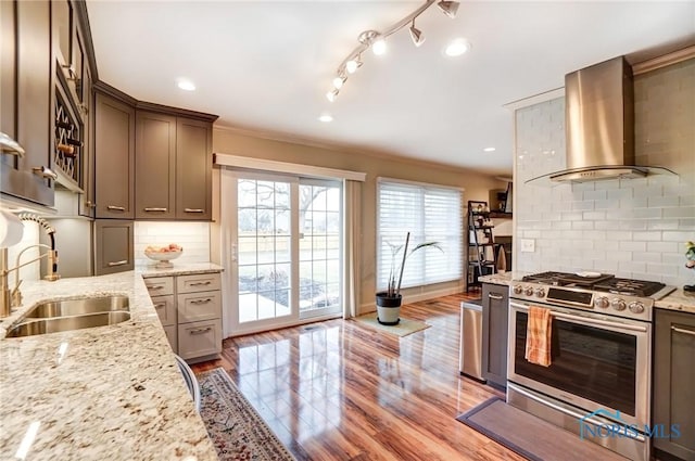 kitchen featuring light stone counters, a sink, backsplash, wall chimney exhaust hood, and stainless steel range with gas stovetop