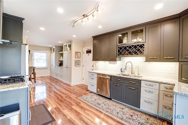 kitchen featuring glass insert cabinets, backsplash, a sink, light wood-type flooring, and stainless steel dishwasher