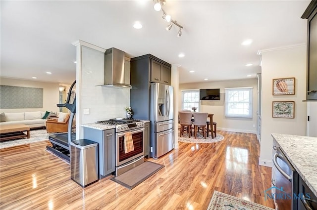 kitchen with light wood finished floors, light stone counters, appliances with stainless steel finishes, wall chimney range hood, and backsplash