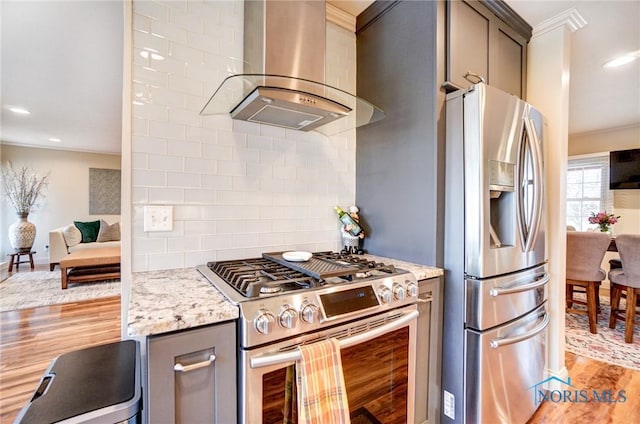 kitchen with crown molding, backsplash, appliances with stainless steel finishes, wall chimney range hood, and light wood-type flooring