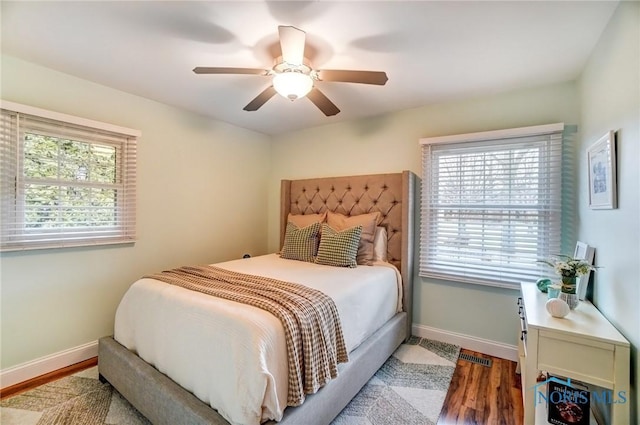 bedroom with a ceiling fan, visible vents, baseboards, and wood finished floors