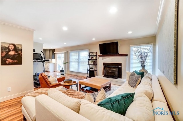 living room featuring light wood finished floors, baseboards, a fireplace with raised hearth, ornamental molding, and recessed lighting