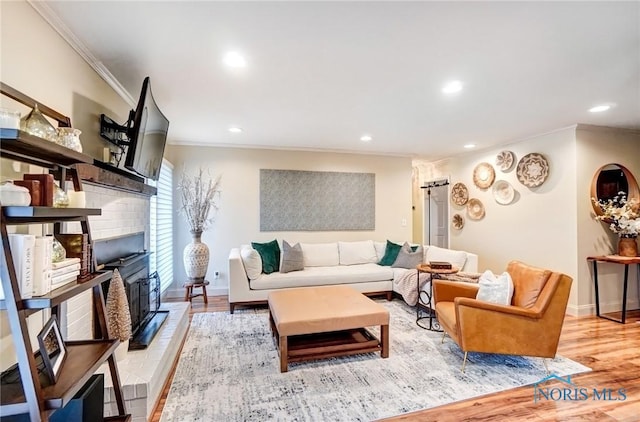 living area featuring recessed lighting, ornamental molding, a brick fireplace, light wood-type flooring, and baseboards