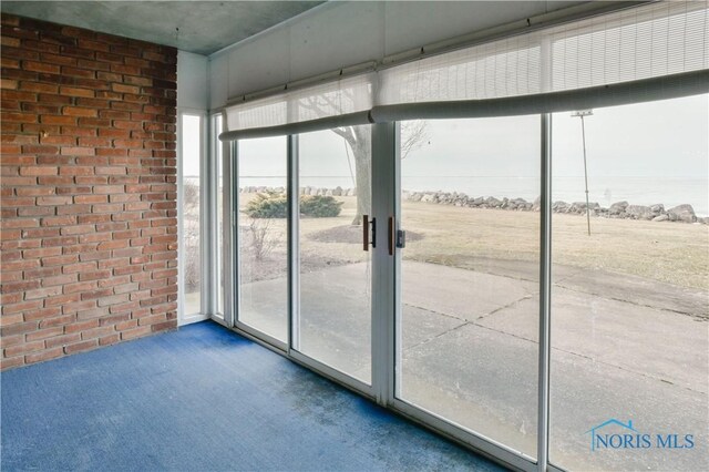 doorway to outside featuring carpet floors and brick wall