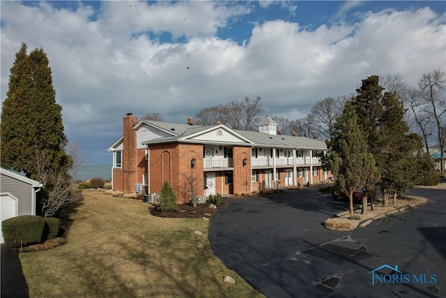 view of front of house with brick siding, a chimney, a front yard, a balcony, and driveway