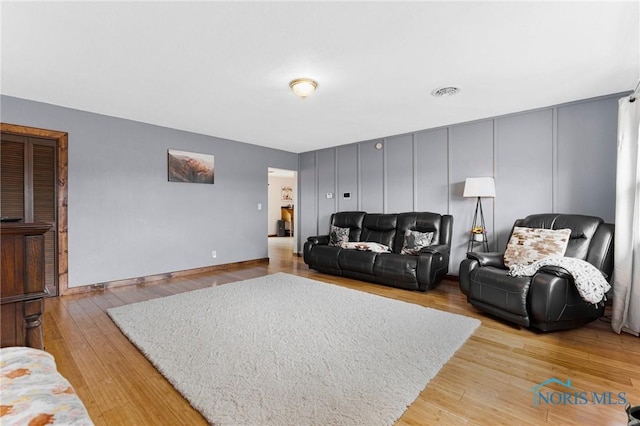 living room featuring visible vents, a decorative wall, light wood-style flooring, and baseboards