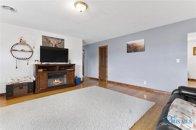 living area featuring a glass covered fireplace, wood finished floors, visible vents, and baseboards