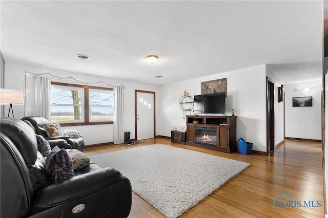 living room featuring baseboards, a glass covered fireplace, visible vents, and light wood-style floors