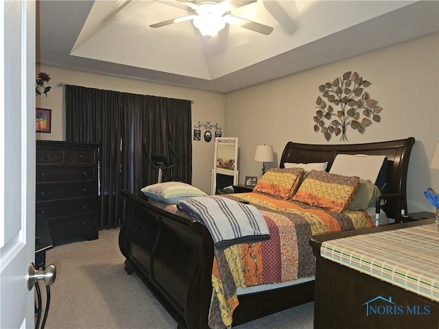 carpeted bedroom featuring a ceiling fan and a raised ceiling