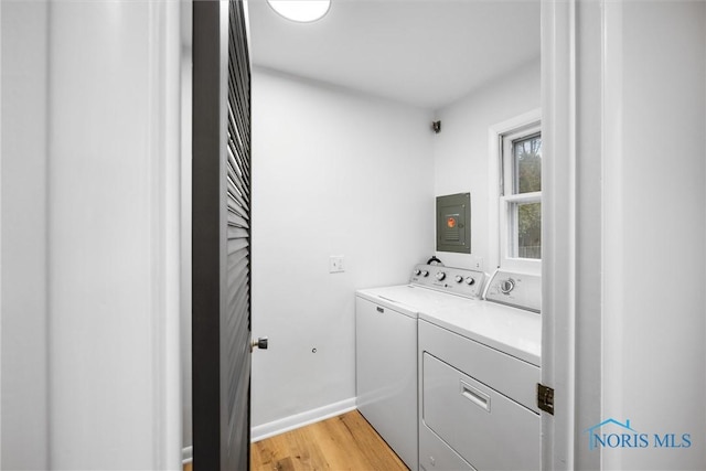 clothes washing area with washing machine and dryer, light wood-type flooring, laundry area, electric panel, and baseboards