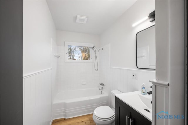 full bathroom with a wainscoted wall, bathing tub / shower combination, wood finished floors, and toilet