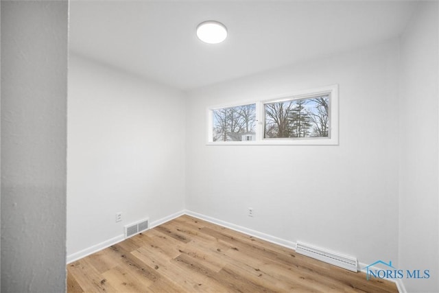 spare room with light wood finished floors, visible vents, and baseboards