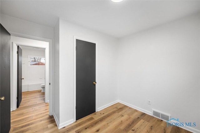 spare room featuring light wood finished floors, visible vents, and baseboards