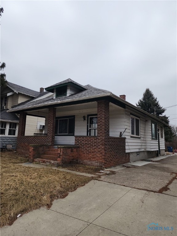 view of front of property featuring covered porch, brick siding, and a chimney