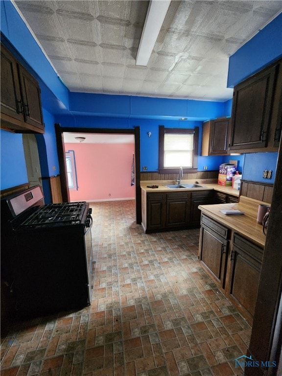 kitchen featuring light countertops, a sink, gas range, and dark brown cabinetry