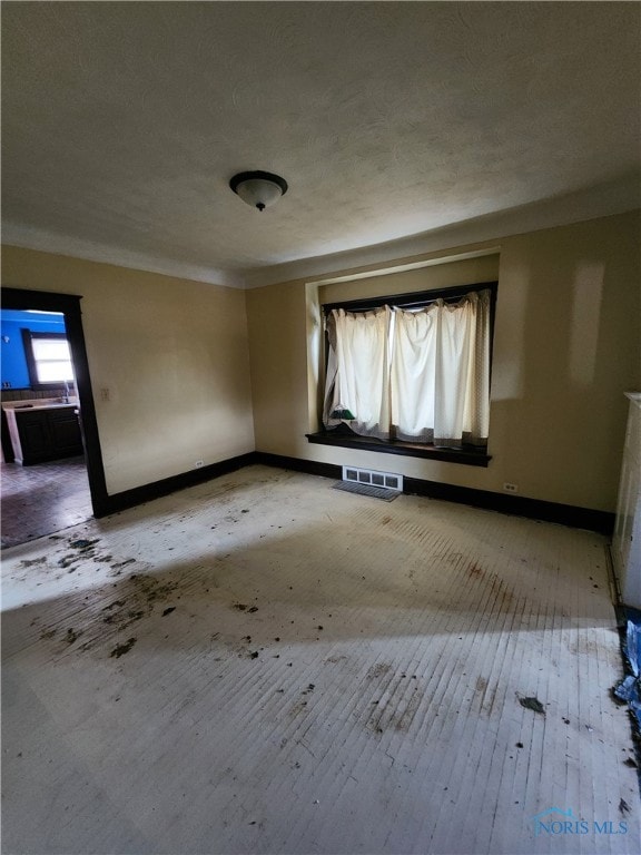 spare room featuring a textured ceiling, light wood-style flooring, visible vents, and baseboards