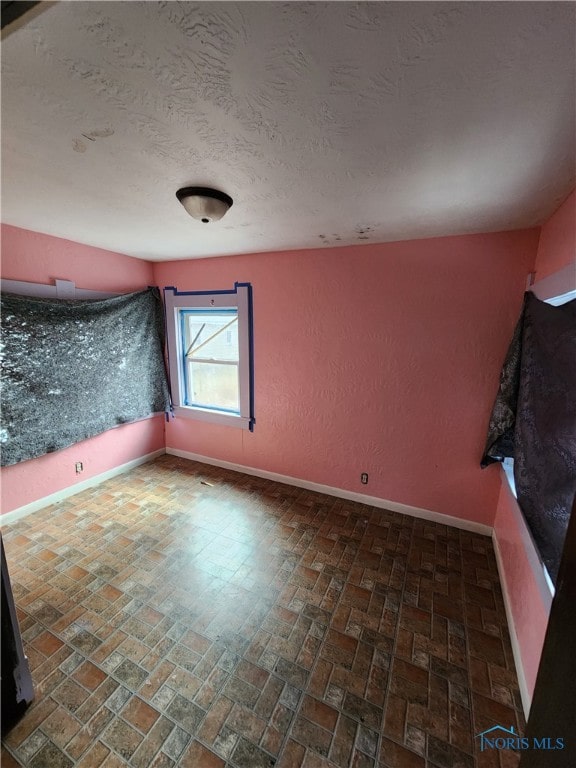 unfurnished room with a textured ceiling, brick floor, and baseboards