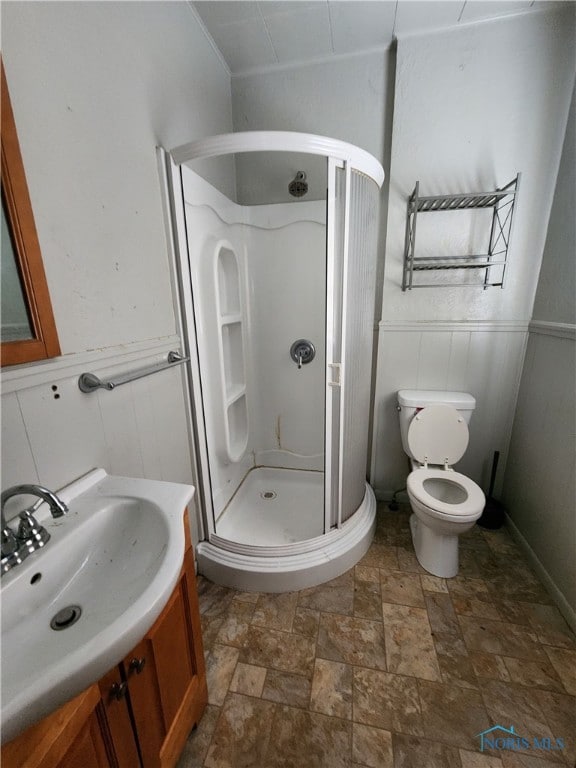 bathroom featuring a wainscoted wall, stone finish flooring, a stall shower, and vanity