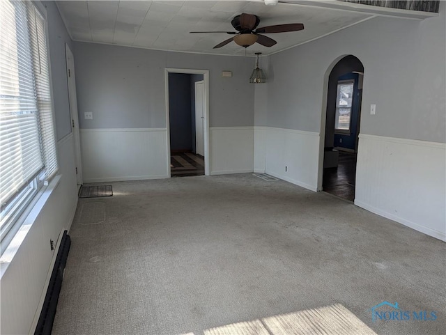 carpeted spare room with a baseboard radiator, arched walkways, ceiling fan, and wainscoting