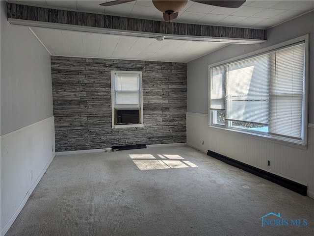 carpeted empty room featuring a baseboard heating unit, a ceiling fan, and a wainscoted wall