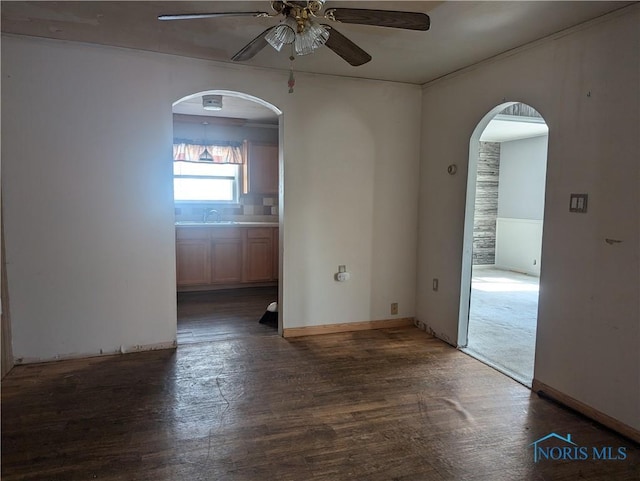 empty room with dark wood-style floors, baseboards, arched walkways, ceiling fan, and a sink