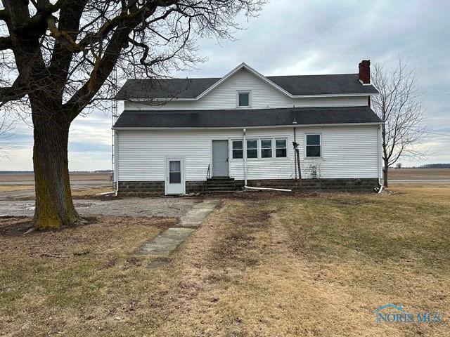 back of house with entry steps, a chimney, and a lawn