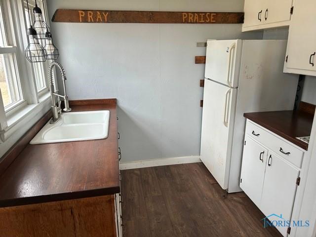 kitchen featuring dark wood-style flooring, a sink, white cabinets, freestanding refrigerator, and dark countertops