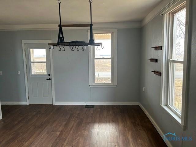 unfurnished dining area with dark wood-type flooring, crown molding, and baseboards