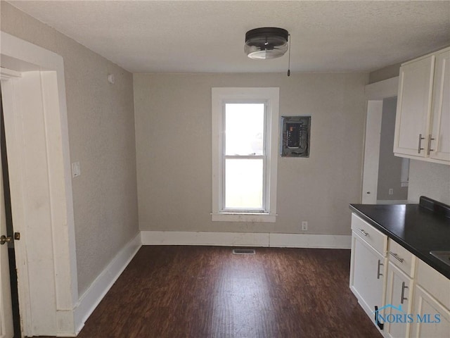 kitchen with dark wood-style floors, dark countertops, white cabinets, and baseboards