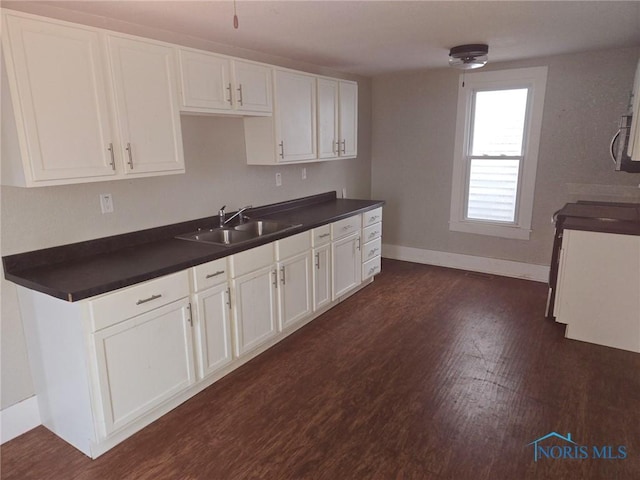 kitchen with dark wood-style flooring, dark countertops, a sink, and white cabinets