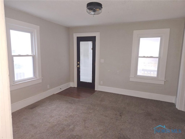 unfurnished room featuring dark carpet and baseboards