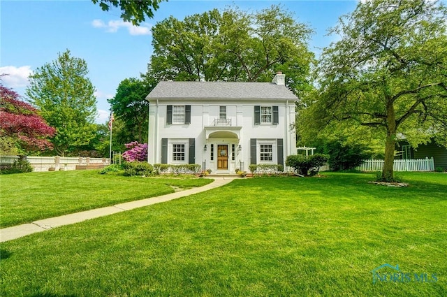 colonial inspired home featuring stucco siding, a chimney, a front lawn, and fence