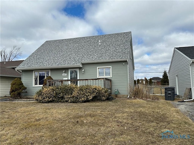 rear view of property featuring roof with shingles, a lawn, and a deck