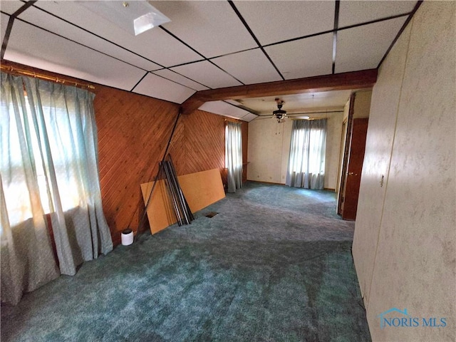 empty room with carpet flooring, wooden walls, and a drop ceiling