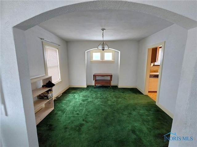 unfurnished dining area with baseboards, arched walkways, and dark carpet