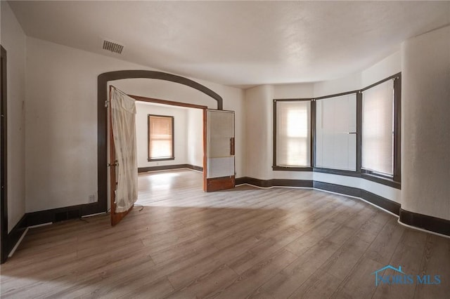 empty room with a healthy amount of sunlight, visible vents, baseboards, and wood finished floors