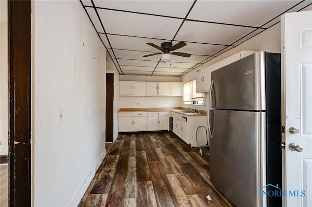 kitchen with dark wood finished floors, a drop ceiling, ceiling fan, freestanding refrigerator, and white cabinetry