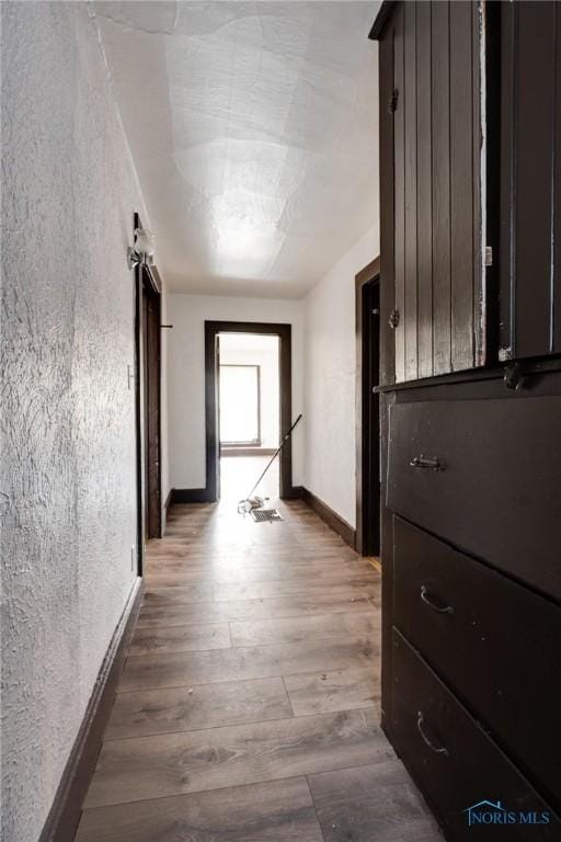 corridor with a textured wall, wood finished floors, and baseboards