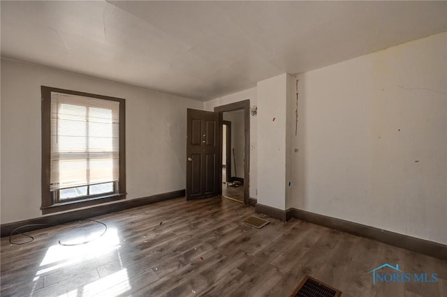 spare room featuring dark wood-type flooring, visible vents, and baseboards