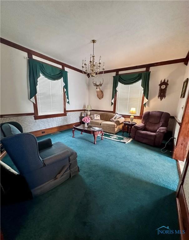 carpeted living area with crown molding, wallpapered walls, wainscoting, and a notable chandelier