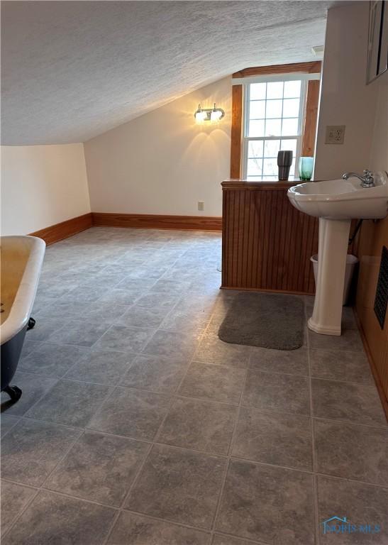 bathroom with vaulted ceiling, a textured ceiling, a sink, and baseboards