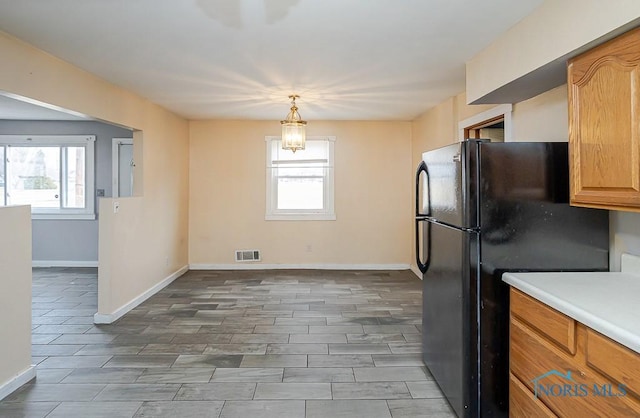 kitchen with light countertops, freestanding refrigerator, visible vents, and baseboards