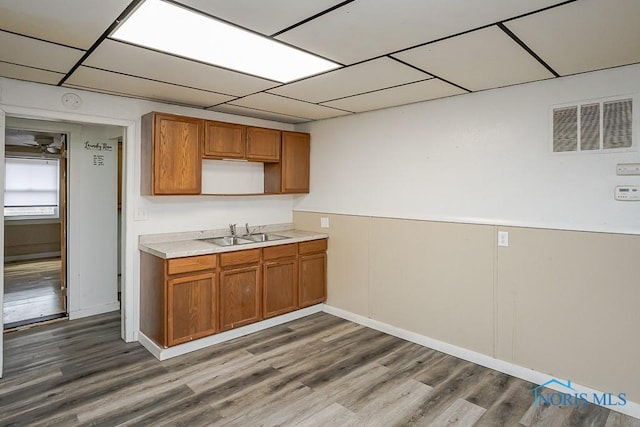 kitchen with brown cabinets, light countertops, visible vents, a sink, and wood finished floors