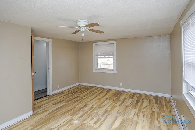 spare room featuring light wood-type flooring, a ceiling fan, baseboards, and a textured ceiling