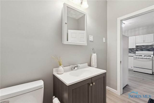 bathroom with toilet, wood finished floors, vanity, baseboards, and backsplash