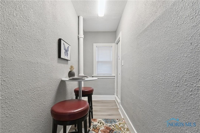 corridor featuring a textured ceiling, a textured wall, wood finished floors, and baseboards