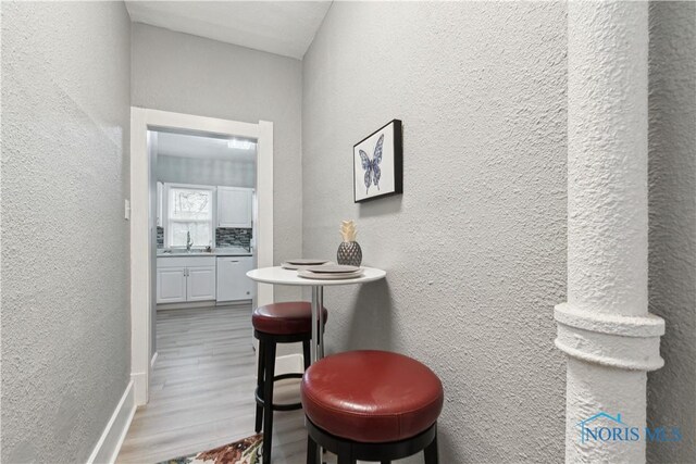 hallway with baseboards, a textured wall, a sink, and wood finished floors