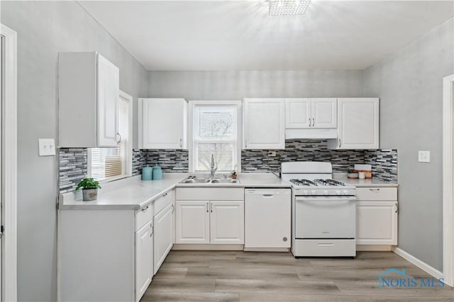 kitchen with white appliances, under cabinet range hood, white cabinetry, and a sink