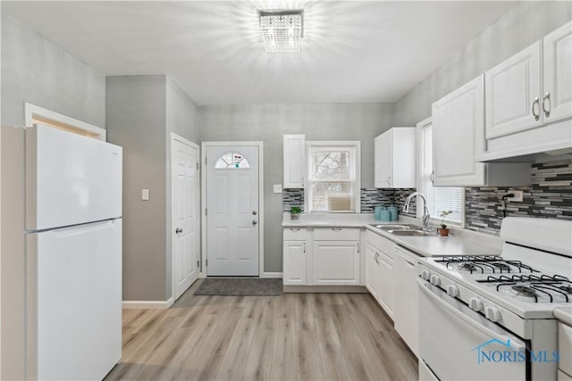 kitchen featuring white appliances, light wood finished floors, white cabinets, light countertops, and a sink