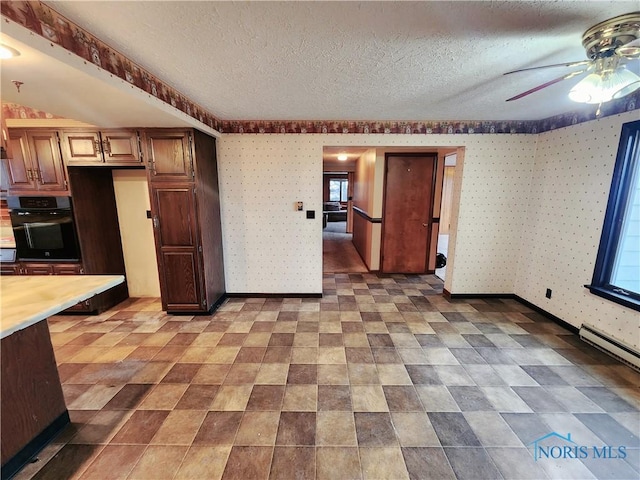 kitchen with wallpapered walls, baseboards, oven, light countertops, and a textured ceiling